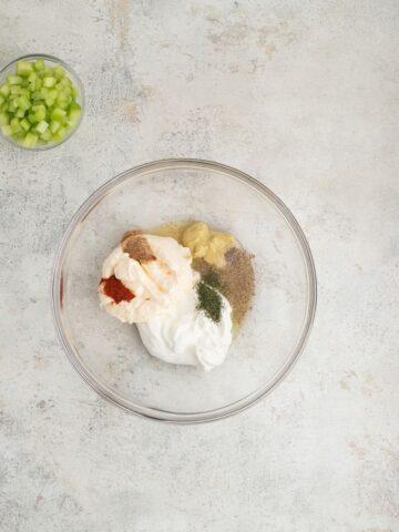 A glass mixing bowl with mayonnaise and seasonings to make simple potato salad without eggs.