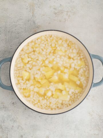 A Dutch oven with diced potatoes, onions, and seasonings to make Potato Salad.