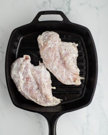 A cast iron grill pan with chicken in a greek yogurt marinade to make grilled chicken gyros.