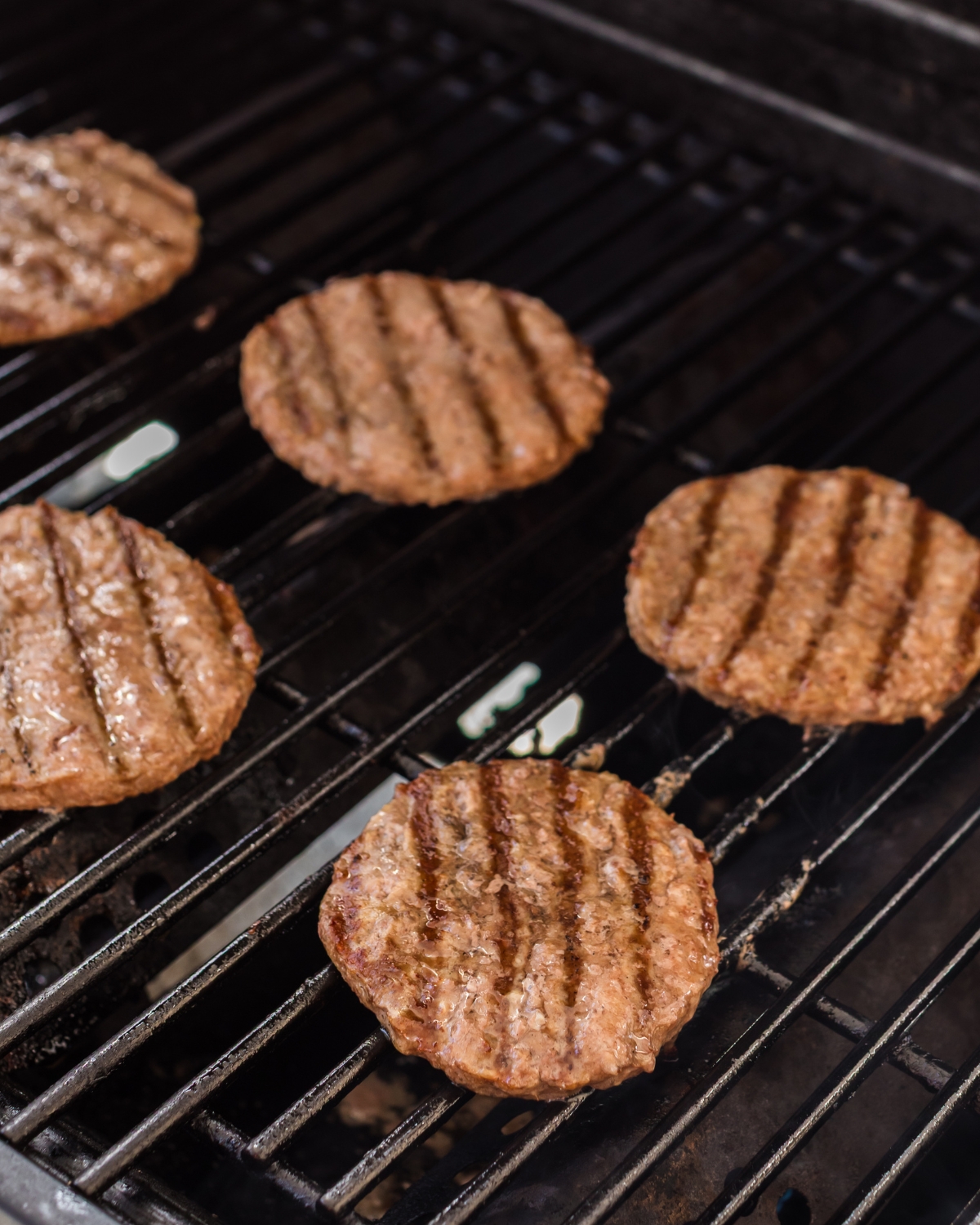 A grill with hamburgers being grilled that were frozen.