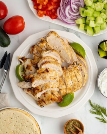 Sliced grilled chicken for gyros on a plate with the topping on another plate.