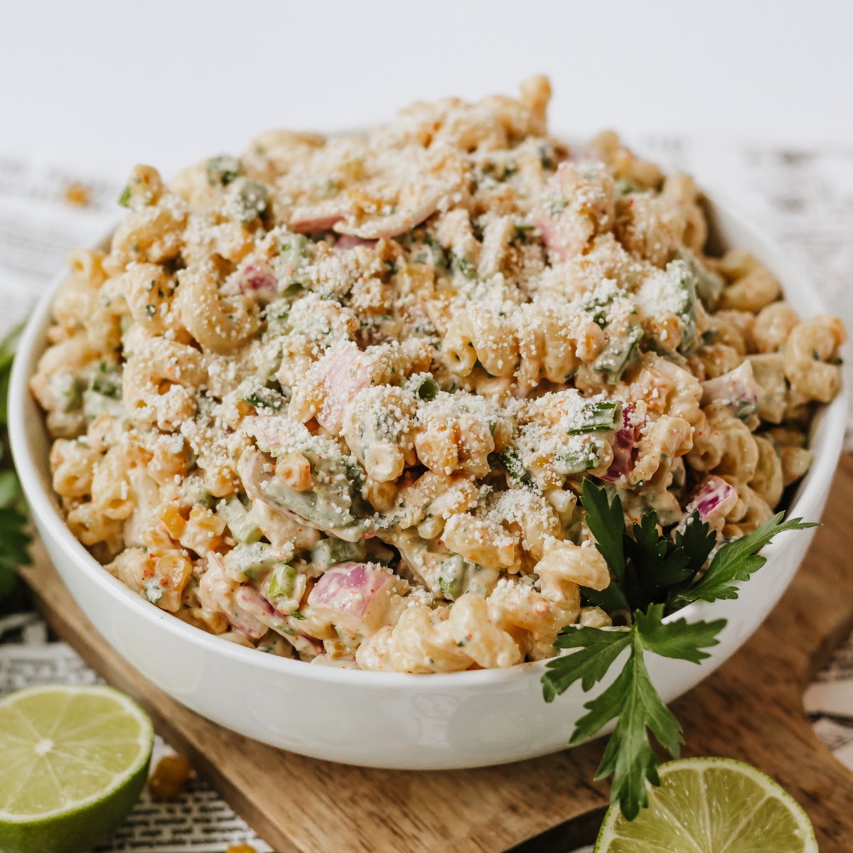 Mexican Corn Salad with cojita cheese in a white bowl topped with fresh cilantro and limes.