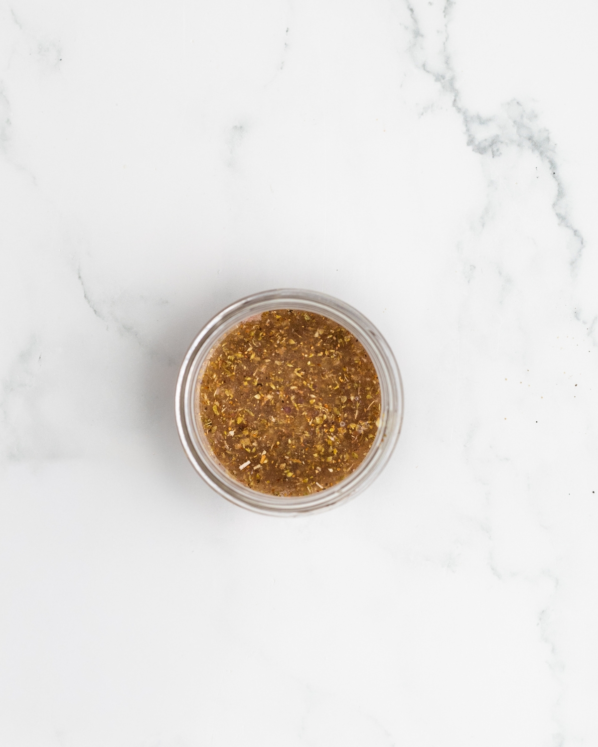 A mason jar with the ingredients for a greek vinaigrette for Greek Orzo Salad.
