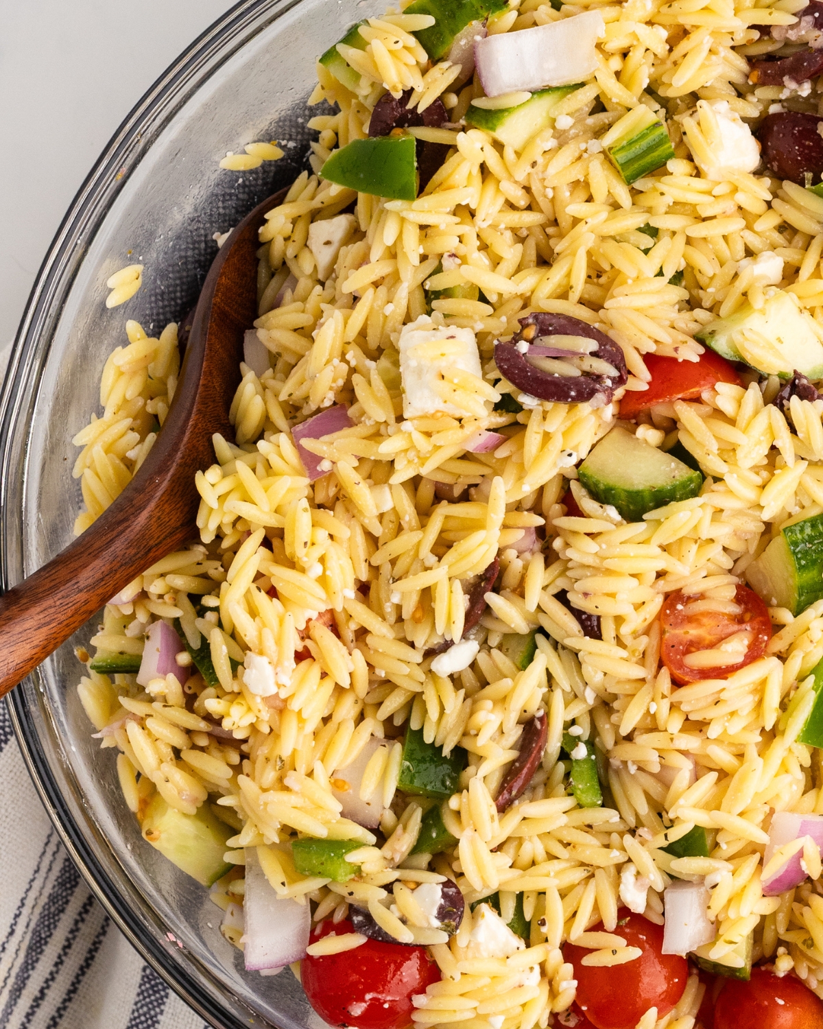 A glass bowl of orzo salad with greek flavors and a lemon greek vinaigrette.