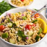 Greek orzo salad with feta in a white bowl with cucumbers, tomatoes, feta, and lemon.