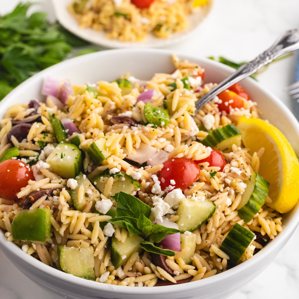 Greek orzo salad with feta in a white bowl with cucumbers, tomatoes, feta, and lemon.