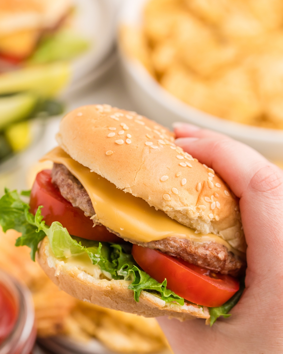 A hand holding a grilled cheeseburger made from frozen on a seeded burger bun with lettuce and tomatoes.