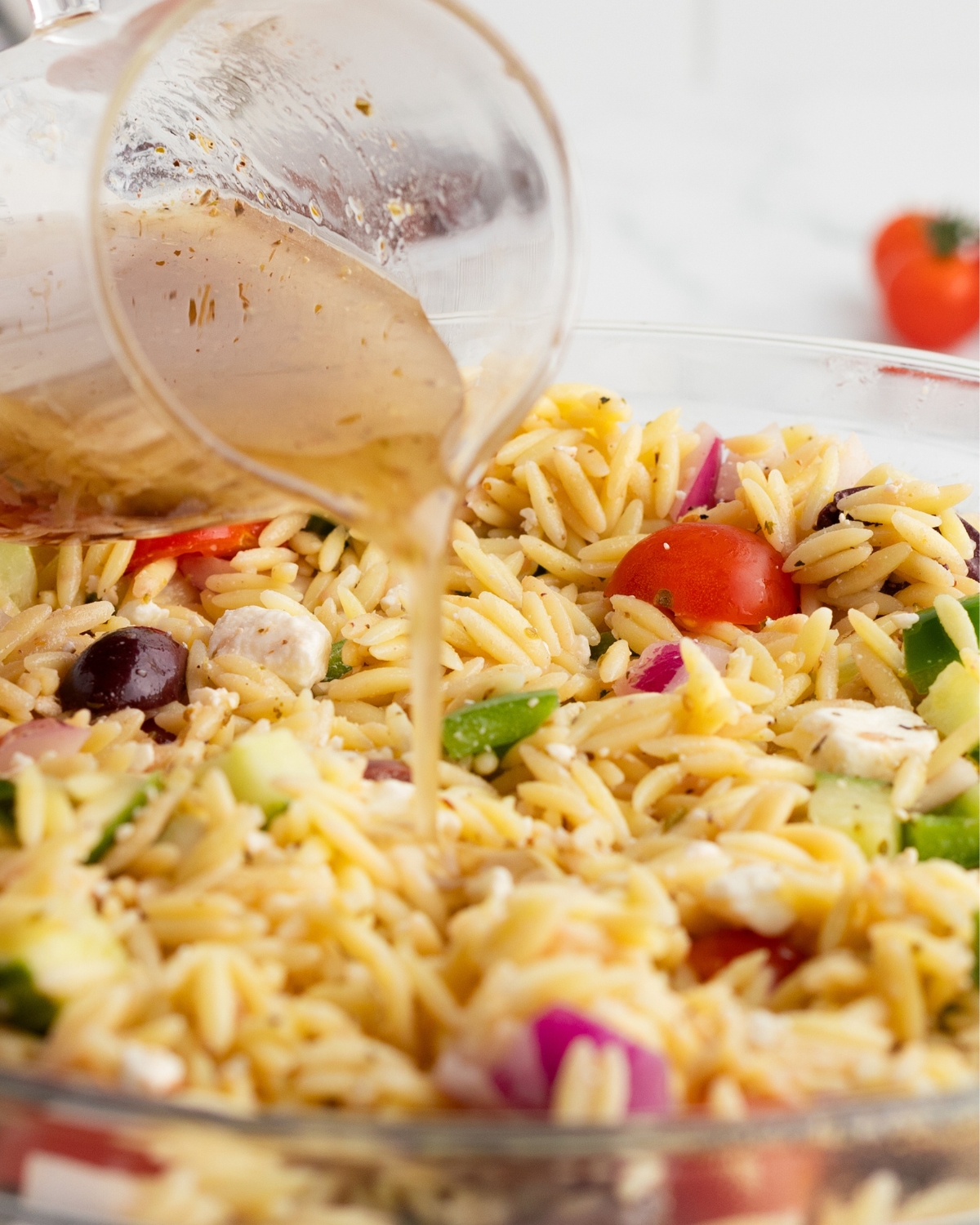 Greek vinaigrette pouring over an orzo salad.