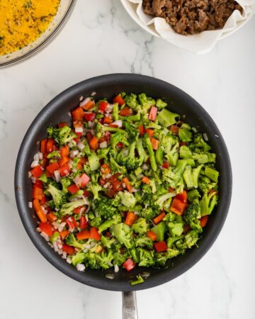 Broccoli, red peppers, and onions in a sauté pan.